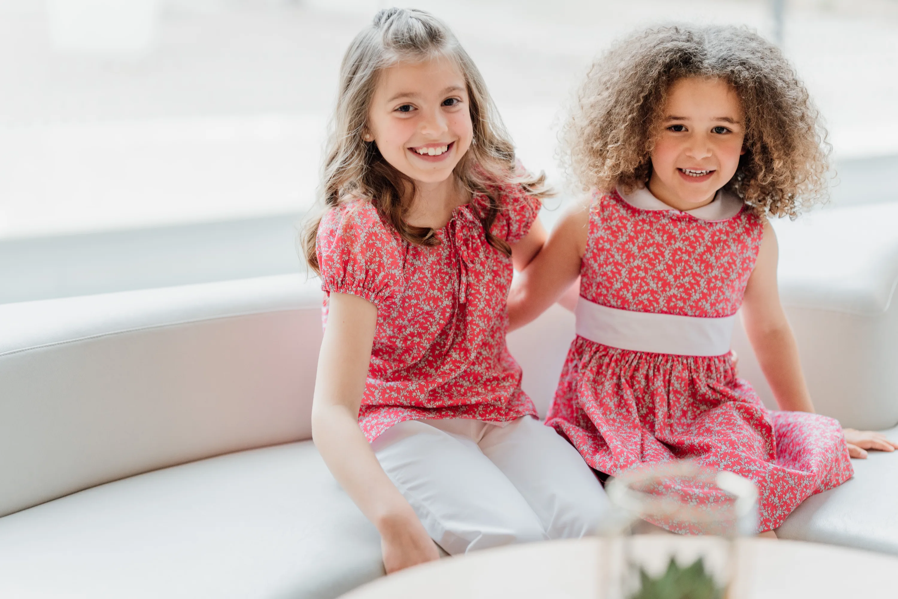 Two young girls sitting together on a couch, smiling.