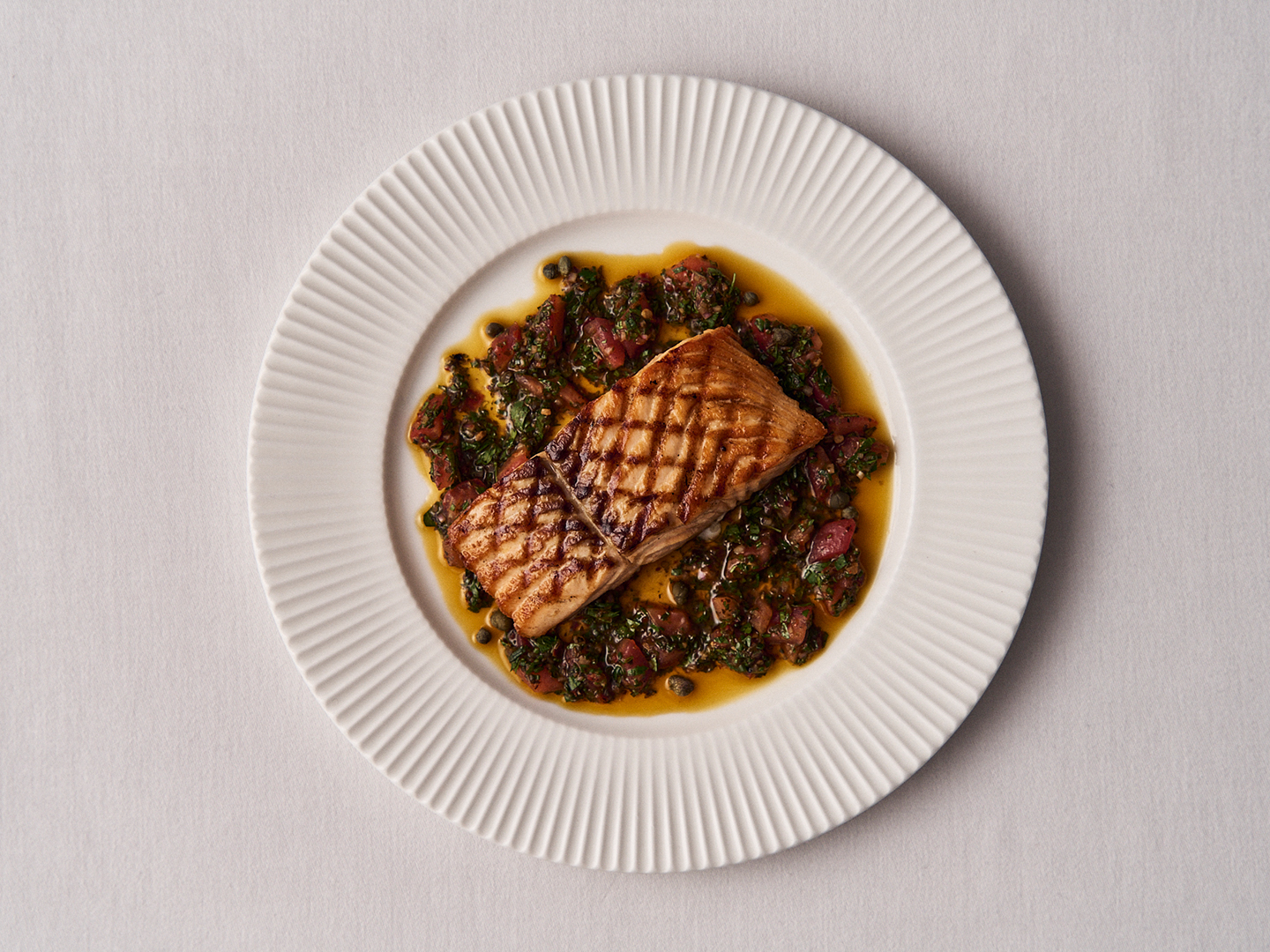 Grilled salmon fillet on a bed of warm herb, tomato and caper sauce
