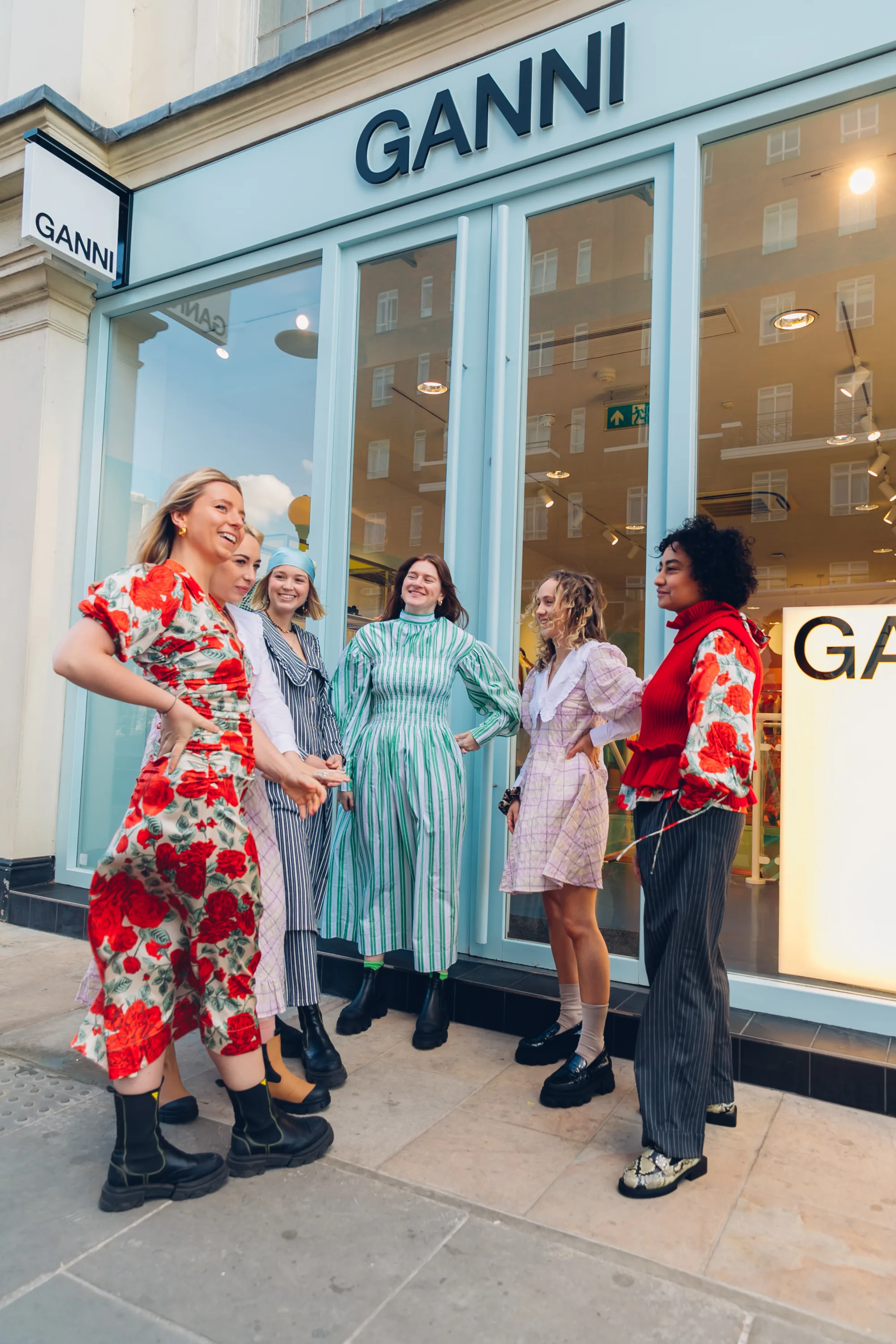 Models wearing Ganni clothing gathered outside a Ganni storefront.