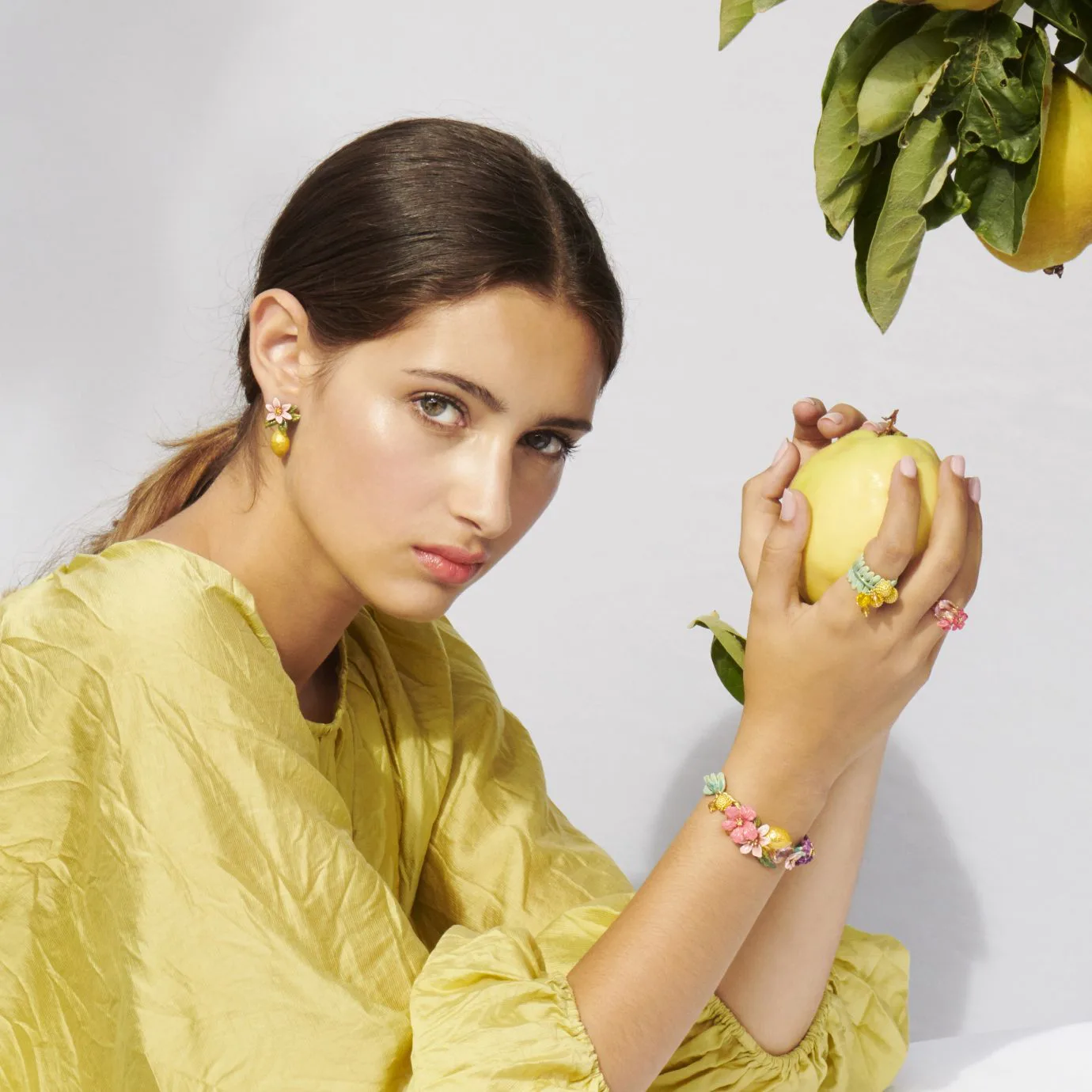 Model showcasing Les Néréides floral jewelry while holding a quince.