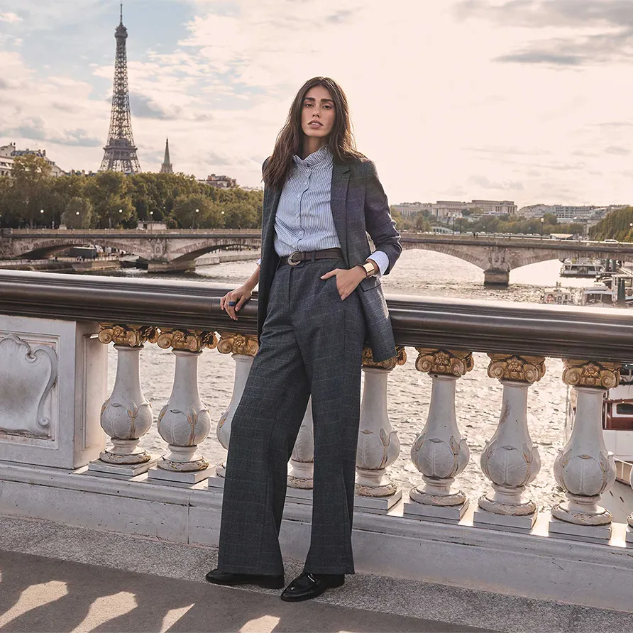 Woman modeling a Maison 123 tailored suit on a Paris bridge overlooking the Seine and the Eiffel Tower.