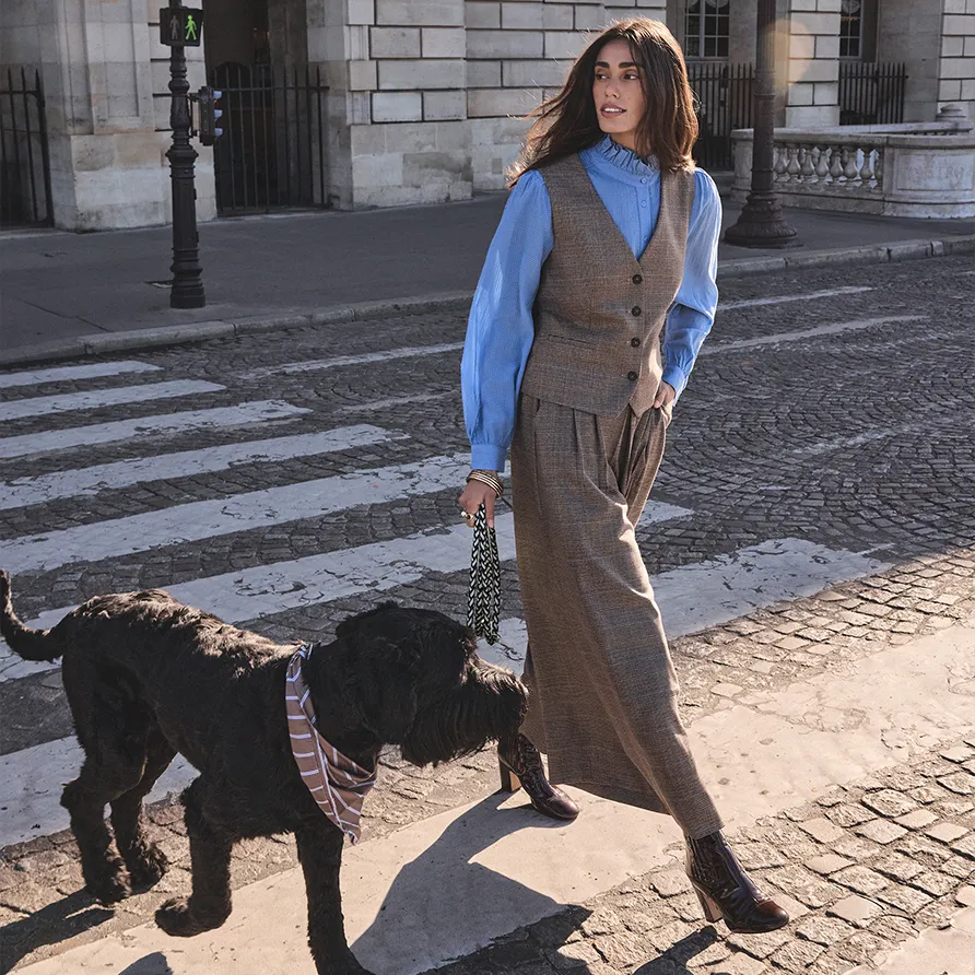 Woman walking a large dog on a city crosswalk modeling a tailored vest and wide-leg trousers