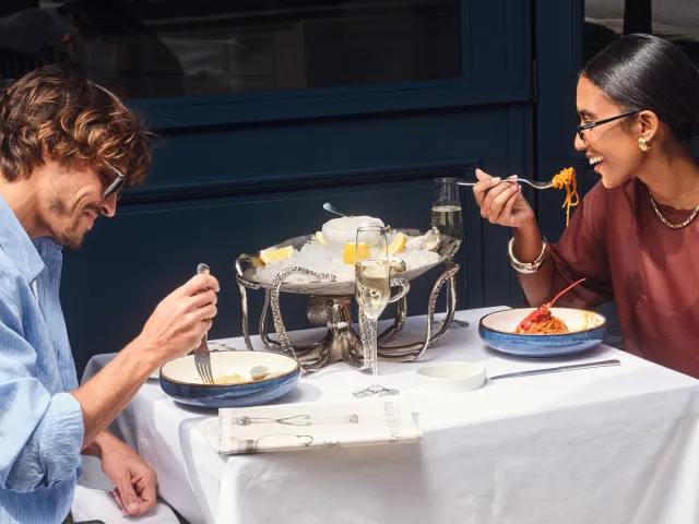 Couple enjoying a relaxed seafood and pasta meal at an outdoor restaurant