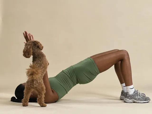 Person doing a glute bridge while interacting with a small dog
