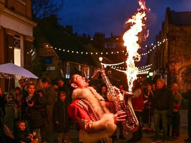 Street performer playing a saxophone that emits flames to entertain an evening Christmas crowd.