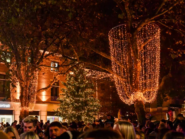 Crowd gathered in Chelsea for an outdoor Christmas celebration beneath illuminated trees.