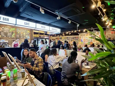 Group paint-and-sip party in a busy indoor art café where participants paint canvases and socialize.