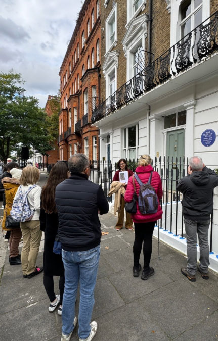 Guided walking tour group gathered outside a Chelsea townhouse with a heritage plaque