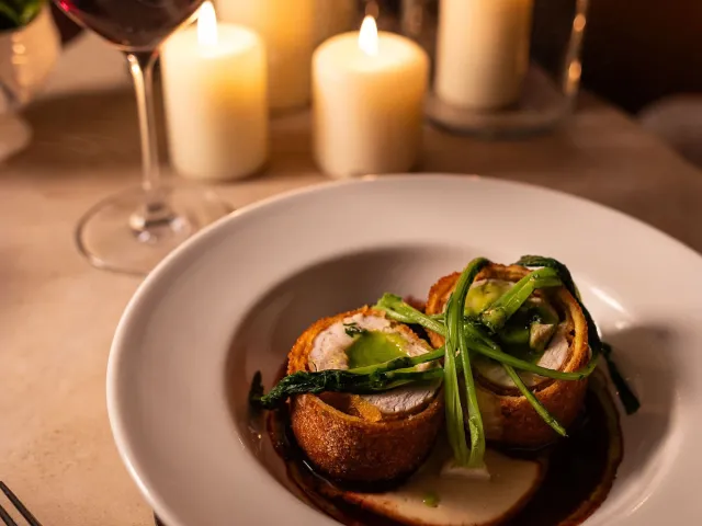 Breaded roulade entrée with green sauce and wilted greens in a candlelit restaurant setting.