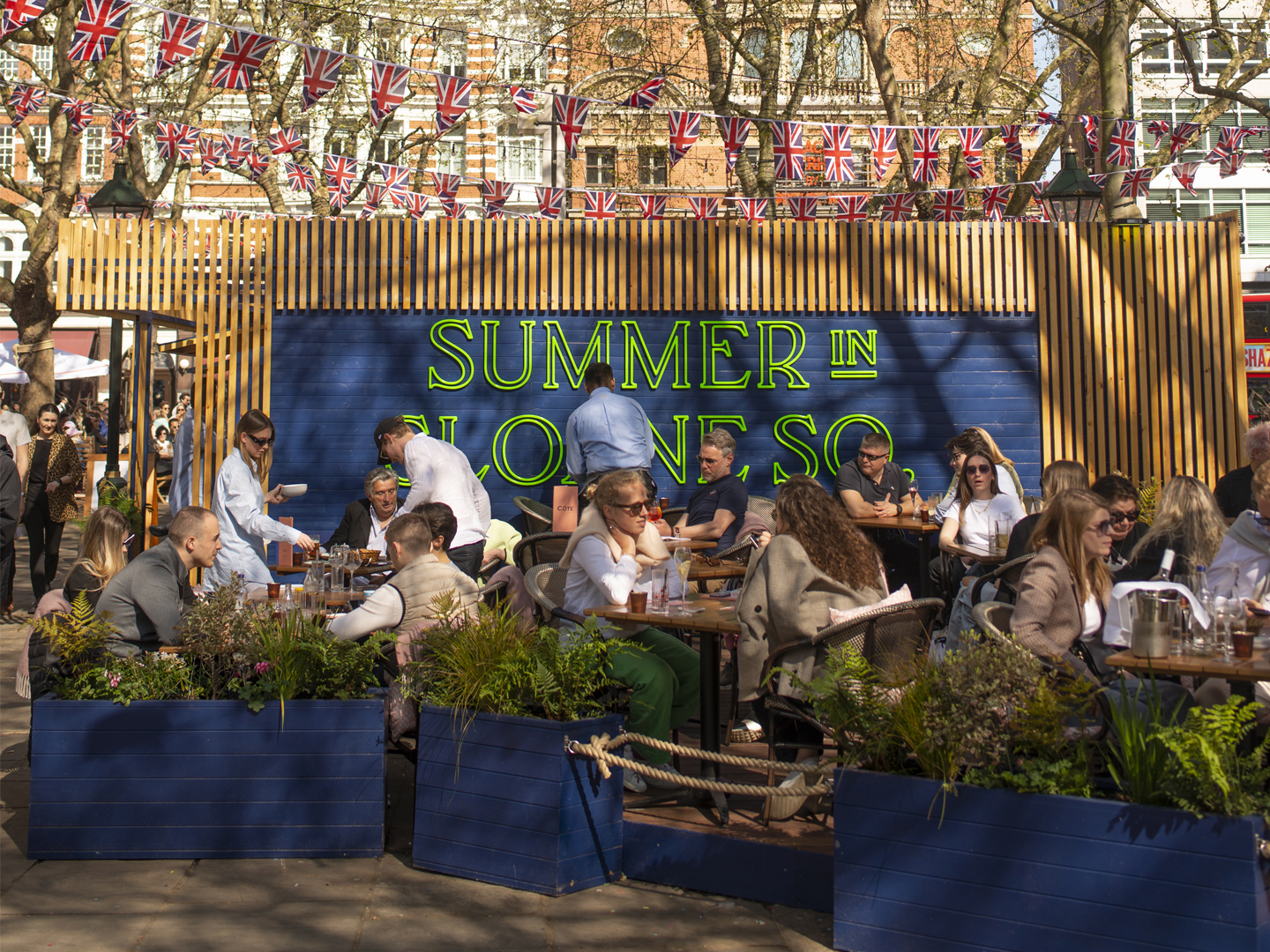 Outdoor dining area promoting Summer in Sloane Square event with people socializing