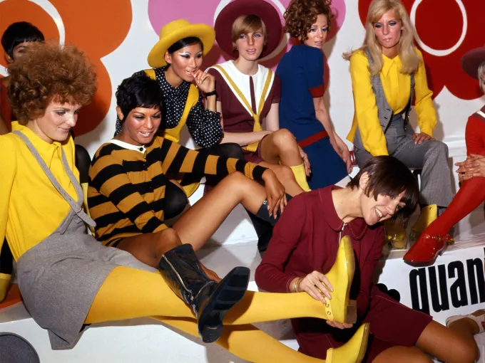 1960s fashion models in a playful group photoshoot trying on boots and showcasing mod clothing.