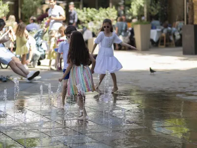 Family enjoying a day out with children playing in a public splash fountain while adults relax nearby.