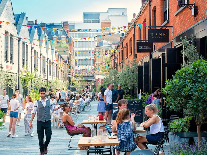 Family-friendly outdoor café terrace at Duke of York Square with people dining under large umbrellas.
