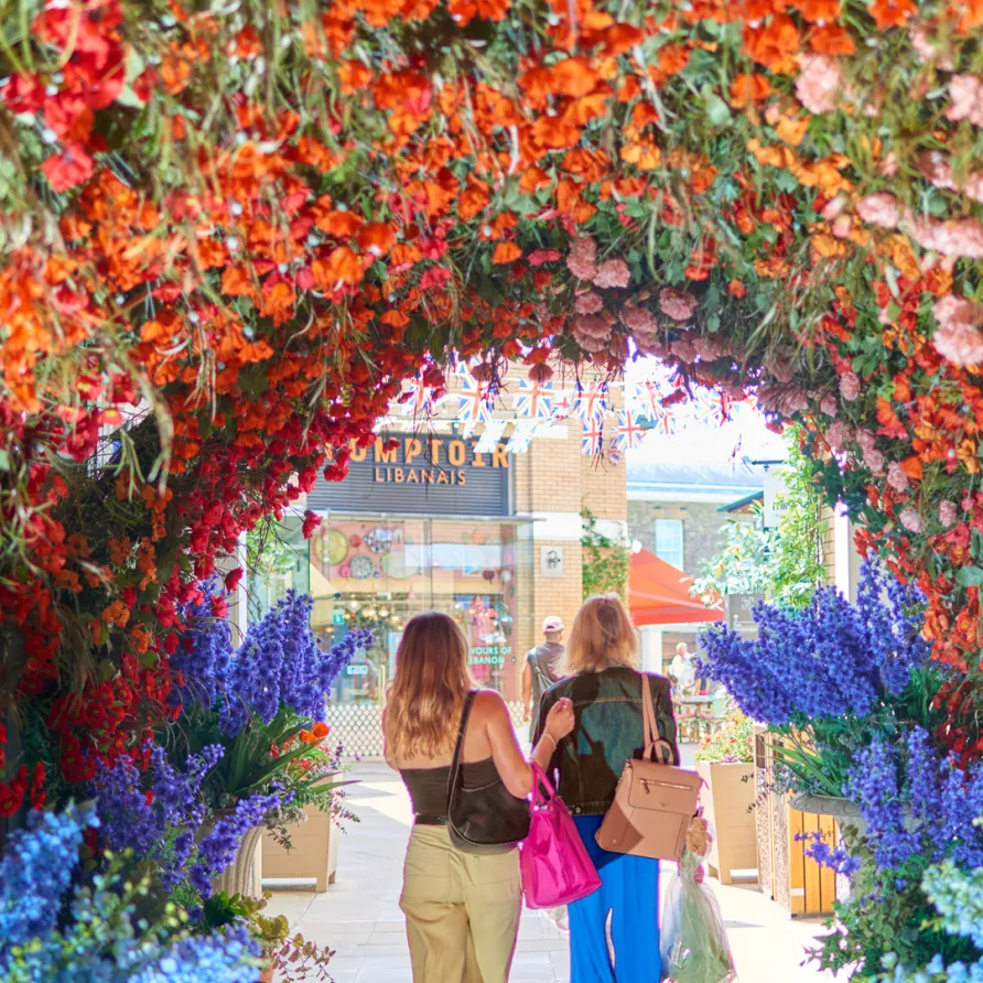 Two visitors walking through a Chelsea in Bloom floral archway
