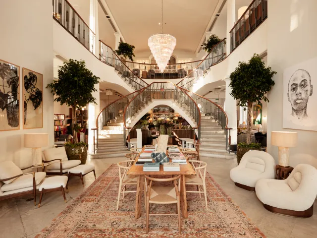 Upscale home goods shop interior presenting curated furniture and decor in a spacious, inviting layout with a central staircase to an upper gallery.