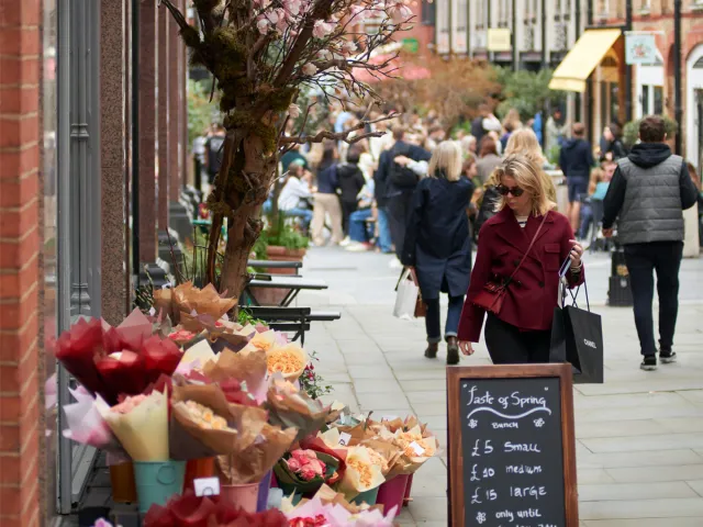 Shopper browsing a sidewalk flower stall on a busy shopping street.